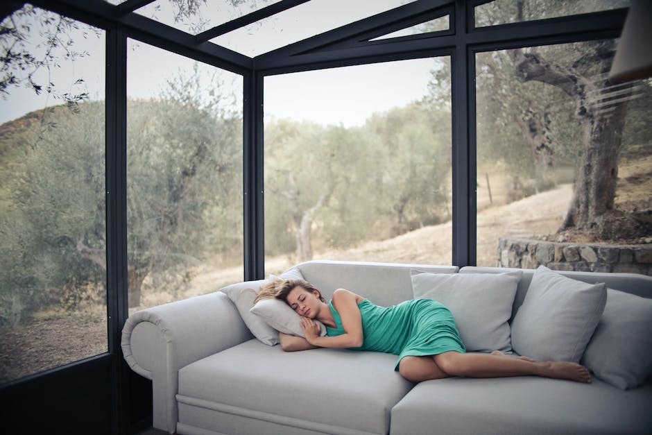 woman sleeps on a couch with a view of trees outside large windows