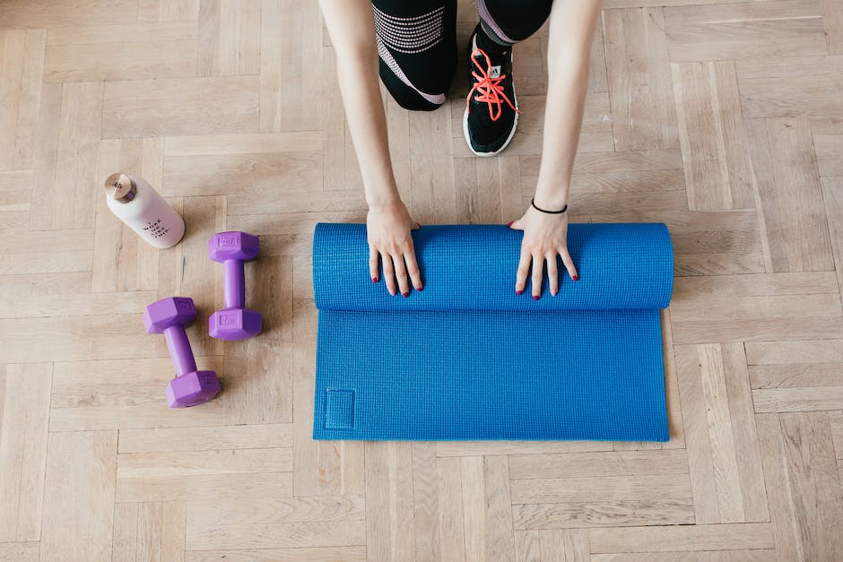 woman hands roll up mattress with purple dumbbells on the left and a white bottle of water 