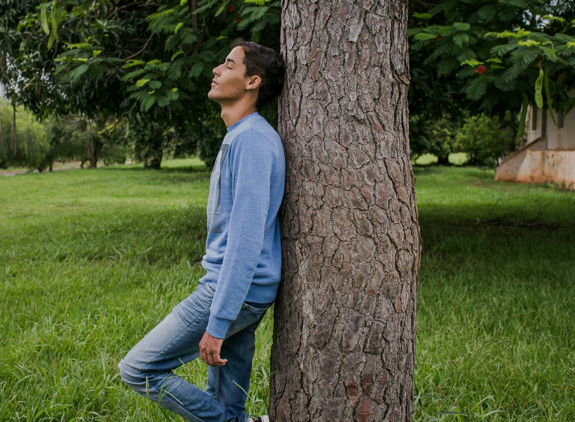 man standing against a tree, closing his eyes and breathing. relaxed.