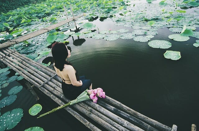 woman-sitting-on-a-wooden-small-bridge-above-water-and-meditating